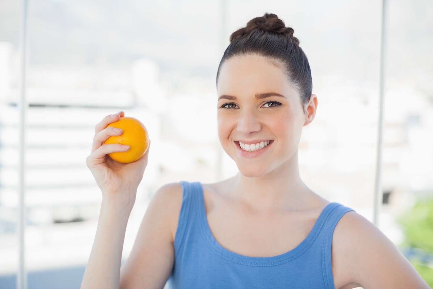 A vibrant woman smiling while holding a fresh orange, symbolizing energy and vitality from B12 injections.