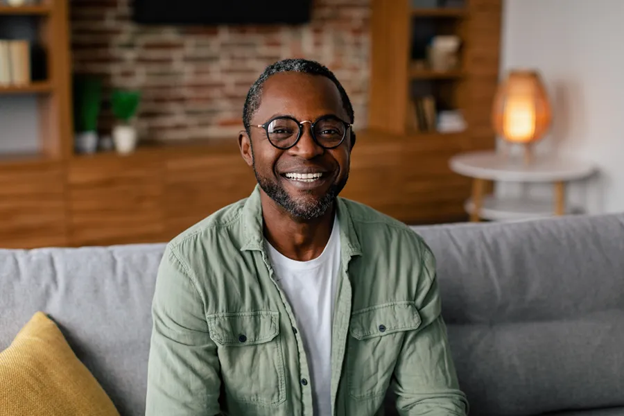 Andropause-Doctor A middle aged black man in a green button up shirt sits on his couch smiling, happy with his treatment for andropause and low testosterone from Guerda Johnson, FNP-C in Tyler East Texas Area.