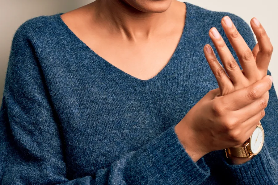 Arthritis-Doctor Close up of a woman in a blue sweater massaging one aching hand with the other. Get help for arthritis from Guerda Johnson, FNP-C in Tyler East Texas Area.