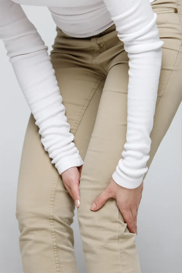 Arthritis-Treatment A woman wearing a white long-sleeve shirt and tan pants, clutching her knee, suffering from arthritis. Get arthritis treatment from Guerda Johnson, FNP-C in Tyler East Texas Area.