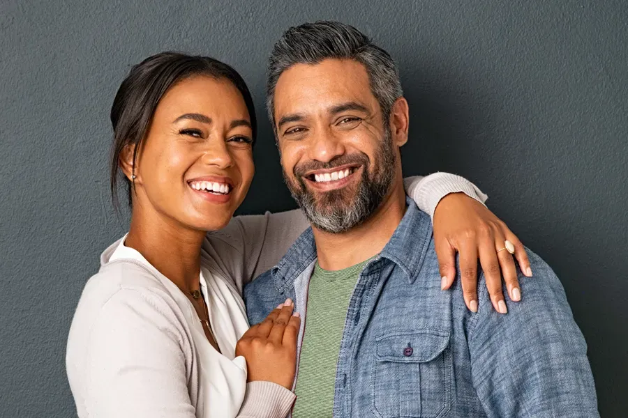 Bioidentical-Hormone-Therapy-Doctor A middle-aged couple with their arms around each other standing against a gray background and smiling, happy with the bioidentical hormone therapy they received from Guerda Johnson, FNP-C in Tyler East Texas Area.