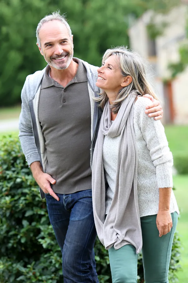 Bioidentical-Hormone-Therapy-Treatment A mature couple in gray toned clothes and jeans walk happily outside, happy with their successful bioidentical hormone treatments from Guerda Johnson, FNP-C in Tyler East Texas Area.