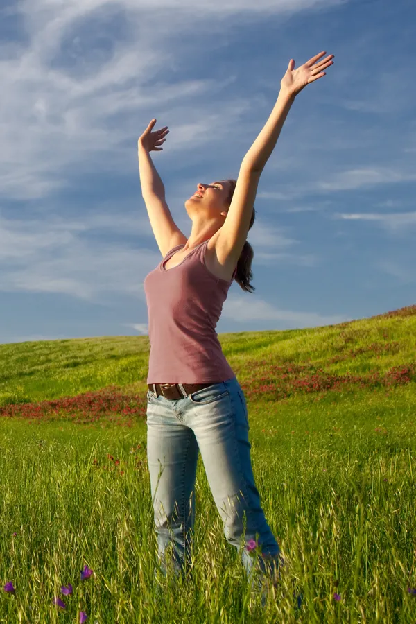 Graves-Disease-Treatment A woman in a tank top and jeans looks up with her arms outstretched to the sky in a field after successful treatment for Grave's Disease from Guerda Johnson, FNP-C in Tyler East Texas Area.