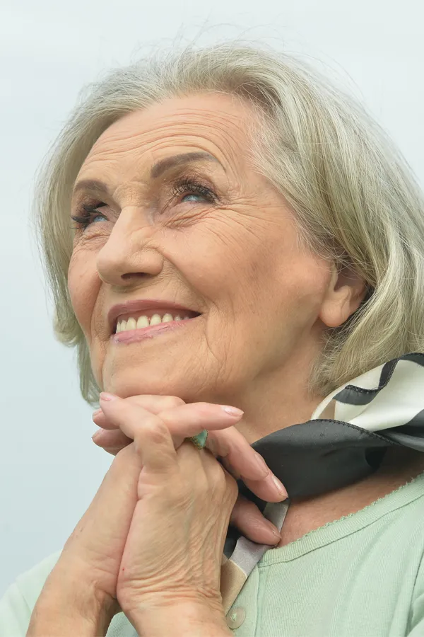 Hot-Flashes-and-Night-Sweats-Treatments An older woman holds her hands together under her chin and looks up at a cool sky smiling. Get treatment for hot flashes and night sweats from Guerda Johnson, FNP-C in Tyler East Texas Area.