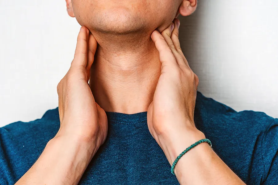 Hypothyroidism-Clinic A man in a dark teal shirt rubs the lymph nodes on his neck. Get hypothyroidism treatment from Guerda Johnson, FNP-C in Tyler East Texas Area.