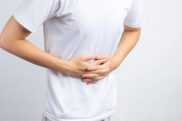 Irritable-Bowel-Syndrome-Clinic A person holding their stomach in visible discomfort against a plain background. Guerda Johnson, FNP-C treats irritable bowel syndrome with functional medicine in Tyler East Texas Area.