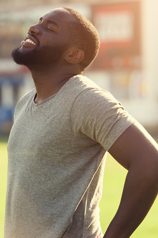 Lean-Muscle-and-Recovery-Treatment A black man in a gray t-shirt and smiles, looking up with closed eyes after a satisfying workout. Get treatment for lean muscle loss and recovery from Guerda Johnson, FNP-C in Tyler East Texas Area.