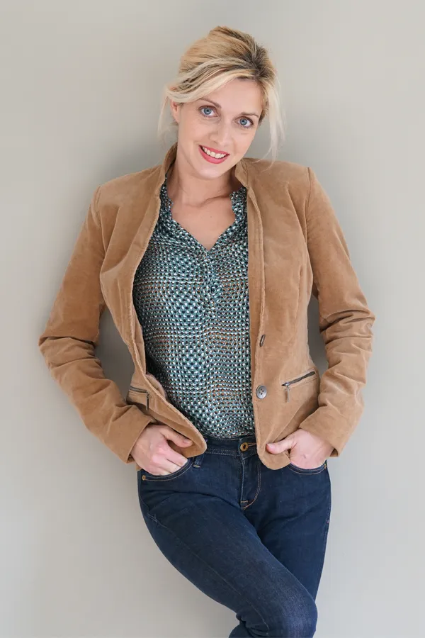 Metabolic-Syndrome-Treatment A smiling blonde woman in a tan leather jacket leans against a gray wall. Schedule metabolic syndrome from Guerda Johnson, FNP-C in Tyler East Texas Area.