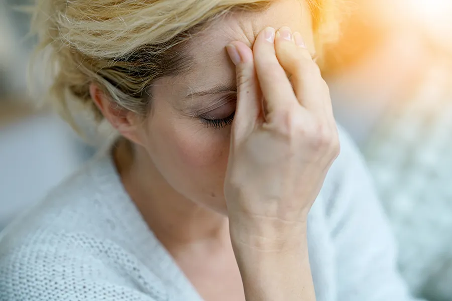 Migraine-and-Chronic-Pain-IV-Therapy-Clinic A woman experiencing a migraine headache pinches her forehead. Schedule IV Therapy for migraine and chronic pain relief from Guerda Johnson, FNP-C in Tyler East Texas Area.