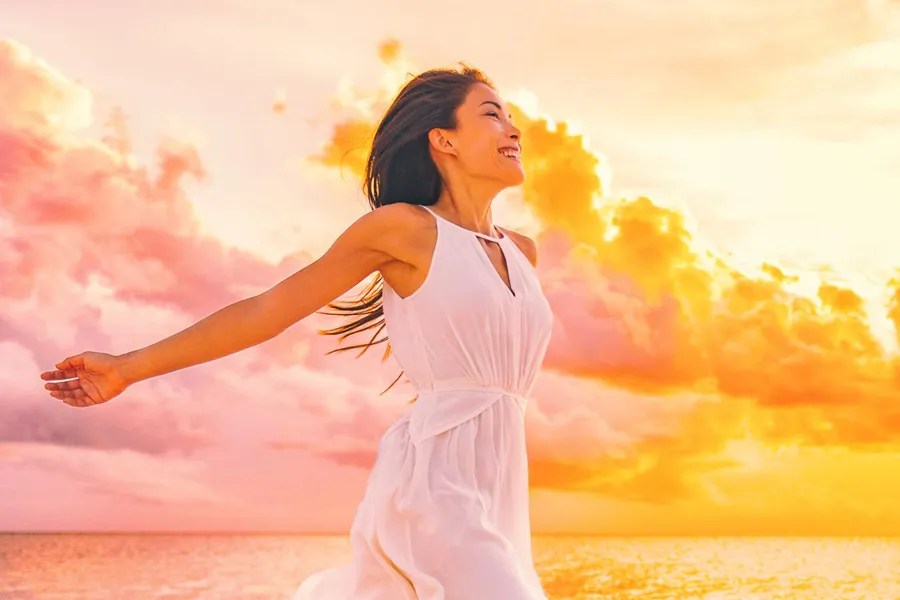 Myers-Cocktail-Clinic A woman in a thin white dress stretches out her arms joyously on the beach at sunrise. Get the Myers Cocktail IV treatment from Guerda Johnson, FNP-C in Tyler East Texas Area.