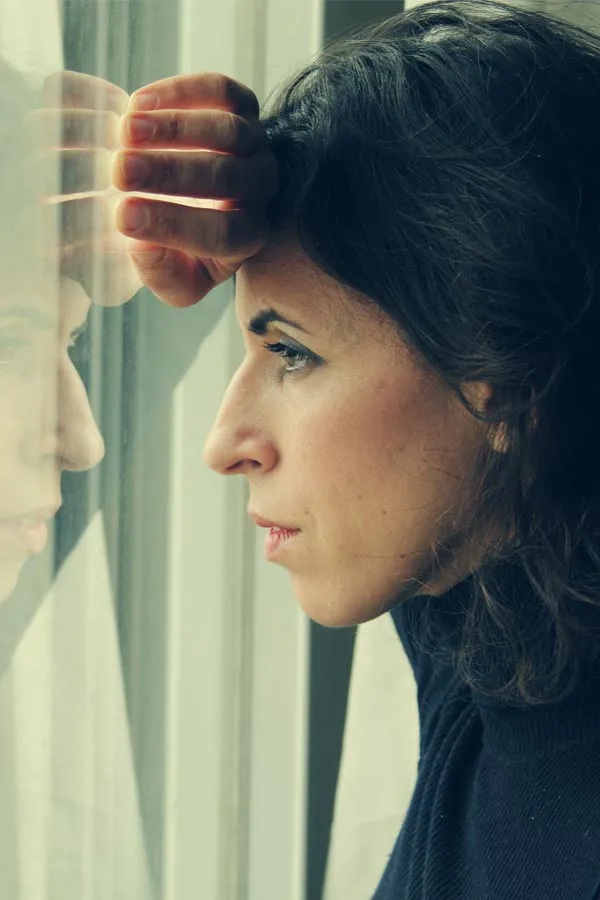 PCOS-Treatment A brunette woman in a thin dark turtleneck looks out the window with a serious expression, suffering from PCOS. Get treatment for Polycistic Ovarian Syndrome/PCOS from Guerda Johnson, FNP-C in Tyler East Texas Area.