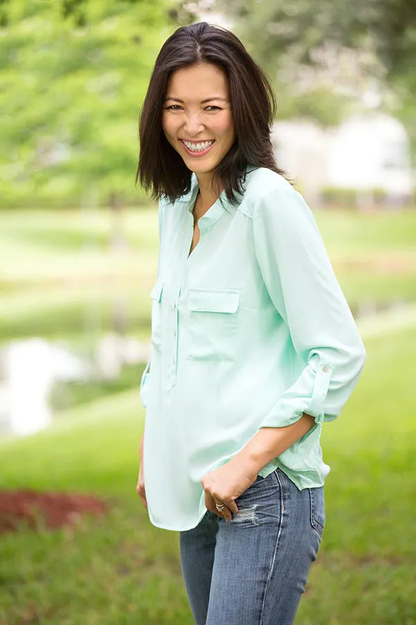 Perimenopause-Treatment A middle-aged brunette woman in a light green button-up shirt stands outside smiling, happy with her perimenopause treatment from Guerda Johnson, FNP-C in Tyler East Texas Area.