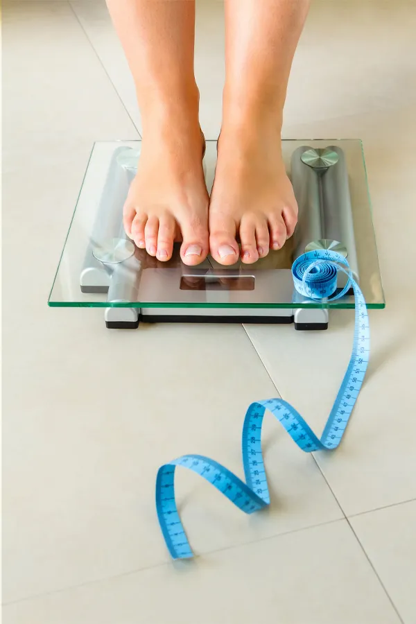 Phendimetrazine-for-Weight-Loss-Treatment A woman standing onto a scale with a tape measure. Get Phendimetrazine for weight loss treatment from Guerda Johnson, FNP-C in Tyler East Texas Area.