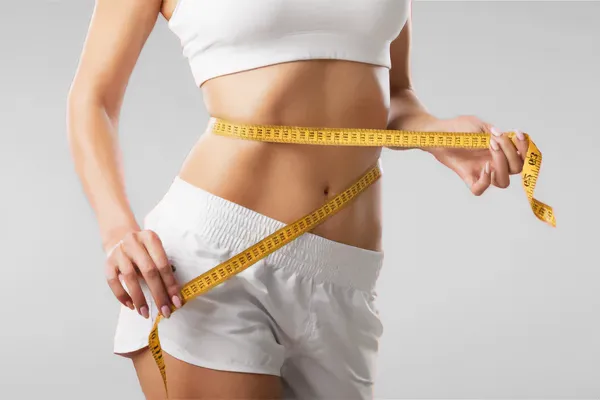 Skinny-Shot-Clinc A woman stands with a tape measure around her waist. Schedule Skinny Shot treatment from Guerda Johnson, FNP-C in Tyler East Texas Area.