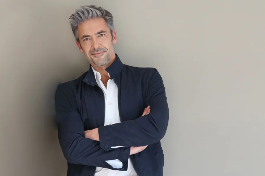 Testosterone-Low-T-Solutionsn-Clinic A middle-aged man in a white shirt and dark blue jacket leans against a gray wall smiling. Get testosterone for Low T from Guerda Johnson, FNP-C in Tyler East Texas Area.